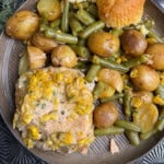 A plate of food with pork chops topped with corn, baby potatoes, green beans, and a piece of cornbread muffin.