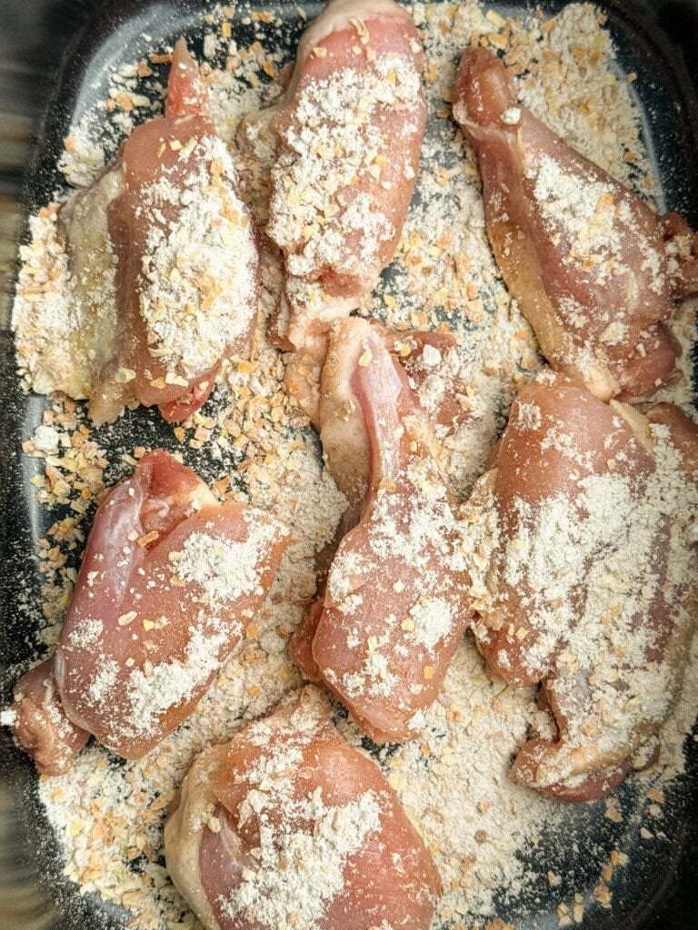 Raw chicken pieces coated with a mixture of onion seasoning, arranged in a black baking tray, ready to be cooked.