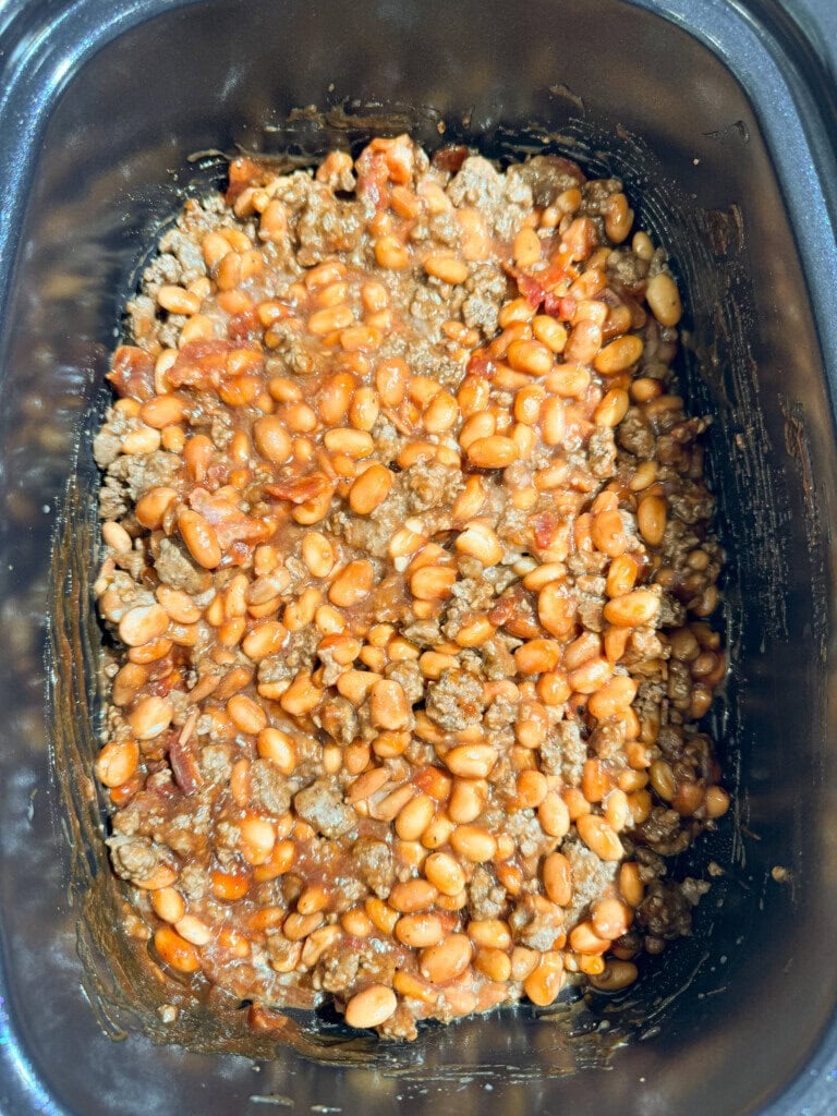 A close-up of baked beans mixed with ground meat and bacon in a slow cooker or crockpot.