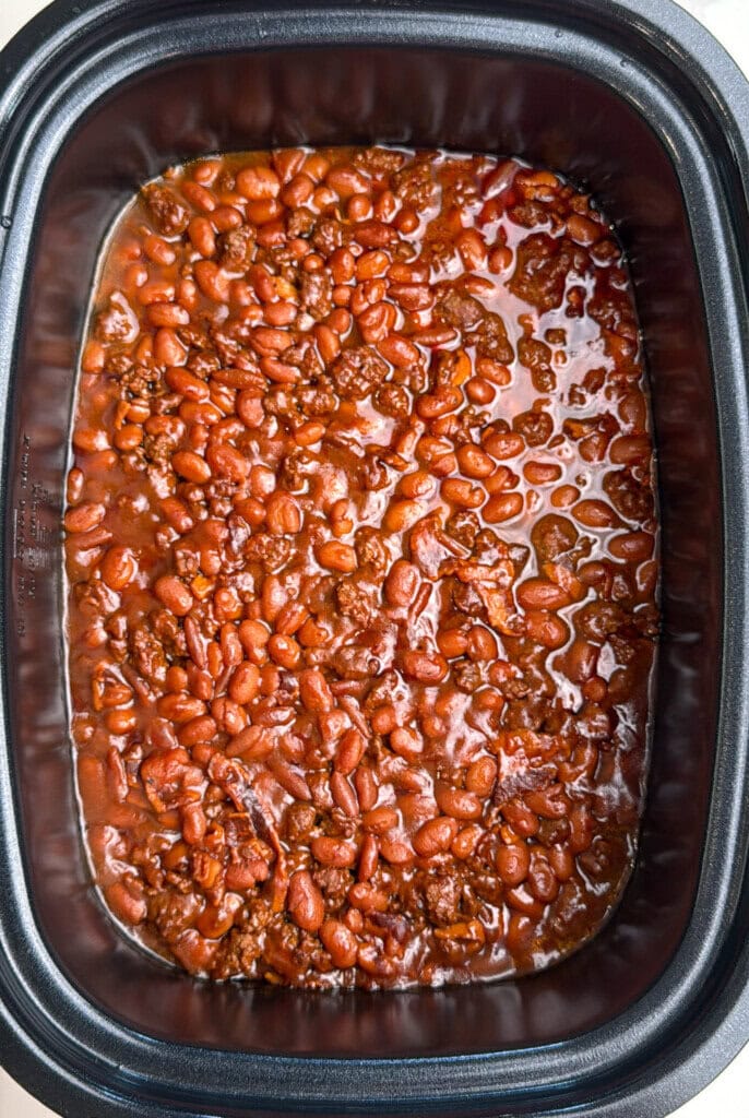 A close-up view of a slow cooker filled with cooked chili, showing pinto beans and ground meat in a rich, reddish-brown sauce.