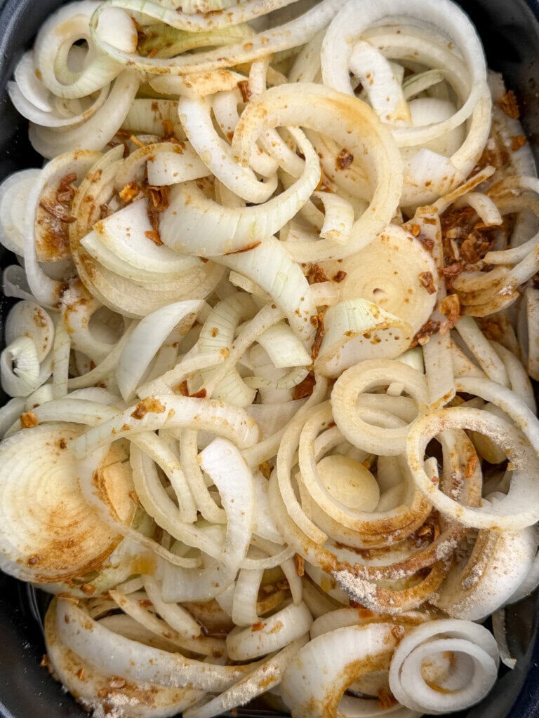 A close-up of sliced raw onions sprinkled with spices and seasonings, showing rings and layers mixed together.
