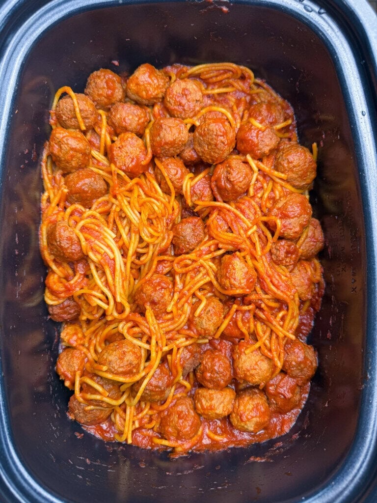 Spaghetti and meatballs mixed in marinara sauce inside a black slow cooker, with the noodles and meatballs spread evenly throughout the dish.