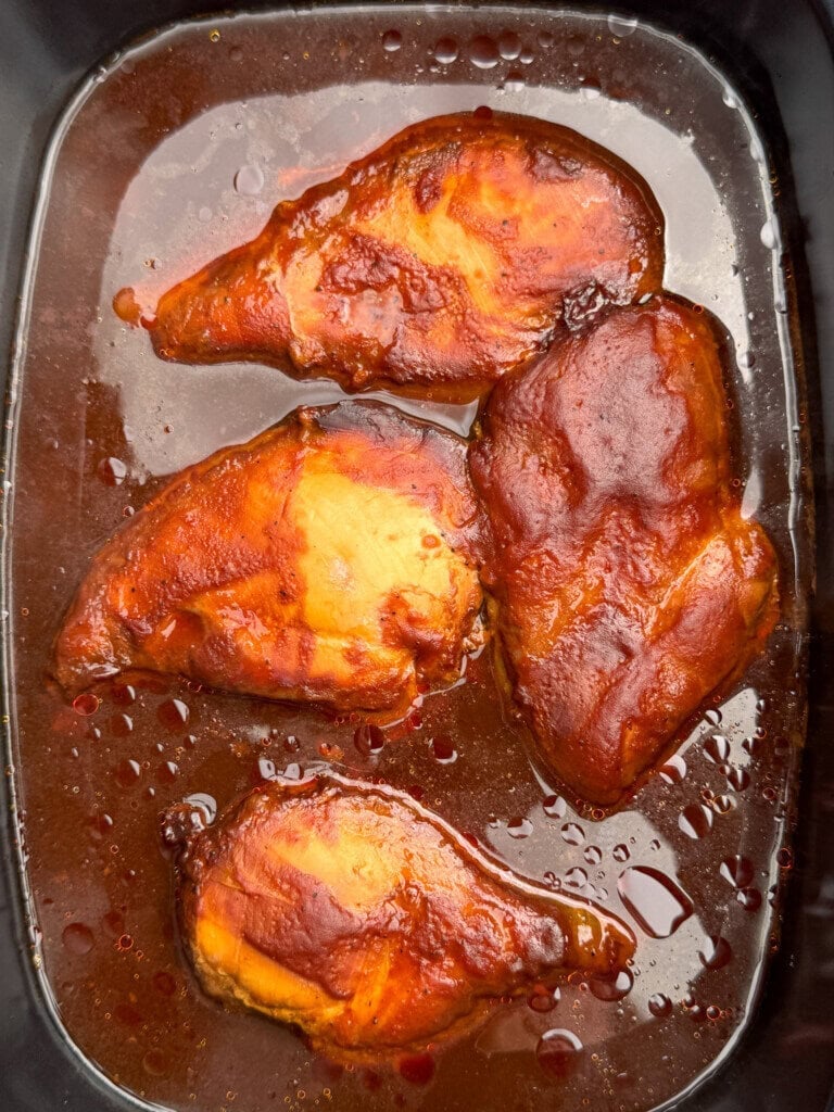 Four glazed chicken breasts in dark, glossy sauce, arranged in a black rectangular dish. The sauce appears thick and rich, coating the chicken pieces evenly.