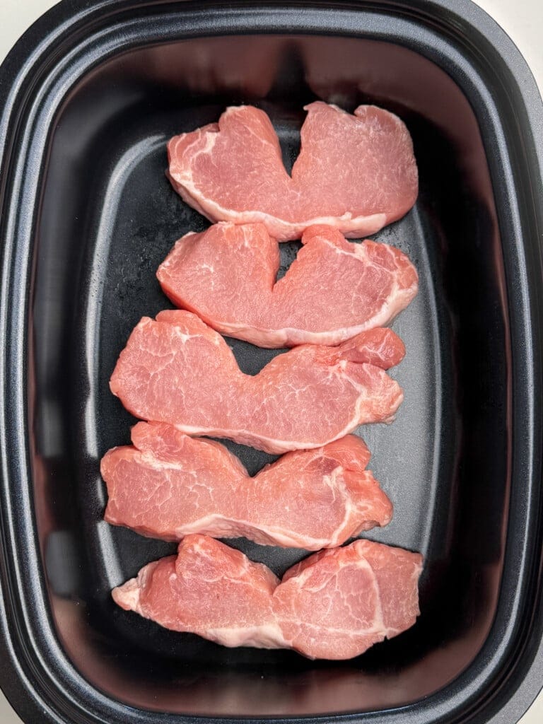 Five raw pork ribs are arranged in a single layer inside a black roasting pan, ready to be cooked.