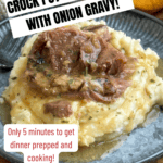A plate of mashed potatoes topped with tender pork steak and rich onion gravy, served with a flaky biscuit. Text reads: Crock Pot Smothered Pork Steaks With Onion Soup Mix! Only 5 minutes to prep. Get the recipe! backtomysouthernroots.com.