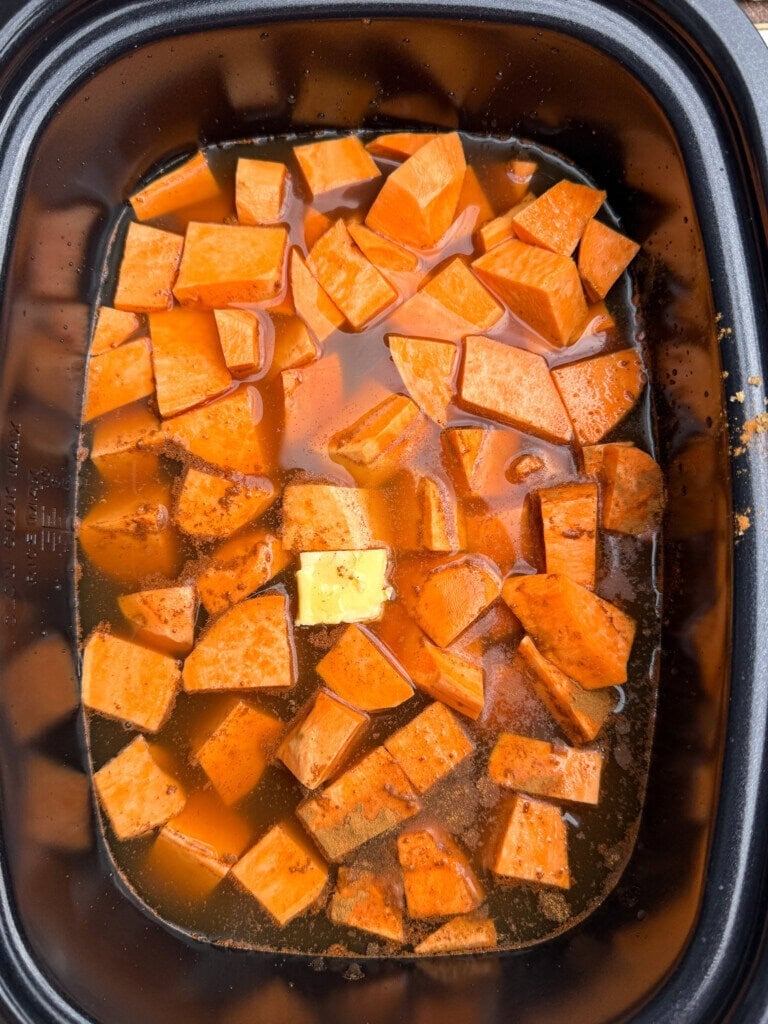 Cubed sweet potatoes in a slow cooker with spices and a pat of butter on top, surrounded by liquid—a simple base for 6-Ingredient Crock Pot Ham And Sweet Potato Soup.