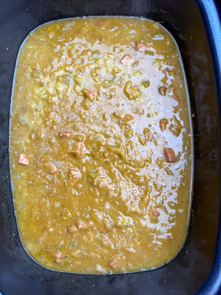 A close-up of thick, yellow-green soup with visible chunks of carrots and celery in a black slow cooker pot.