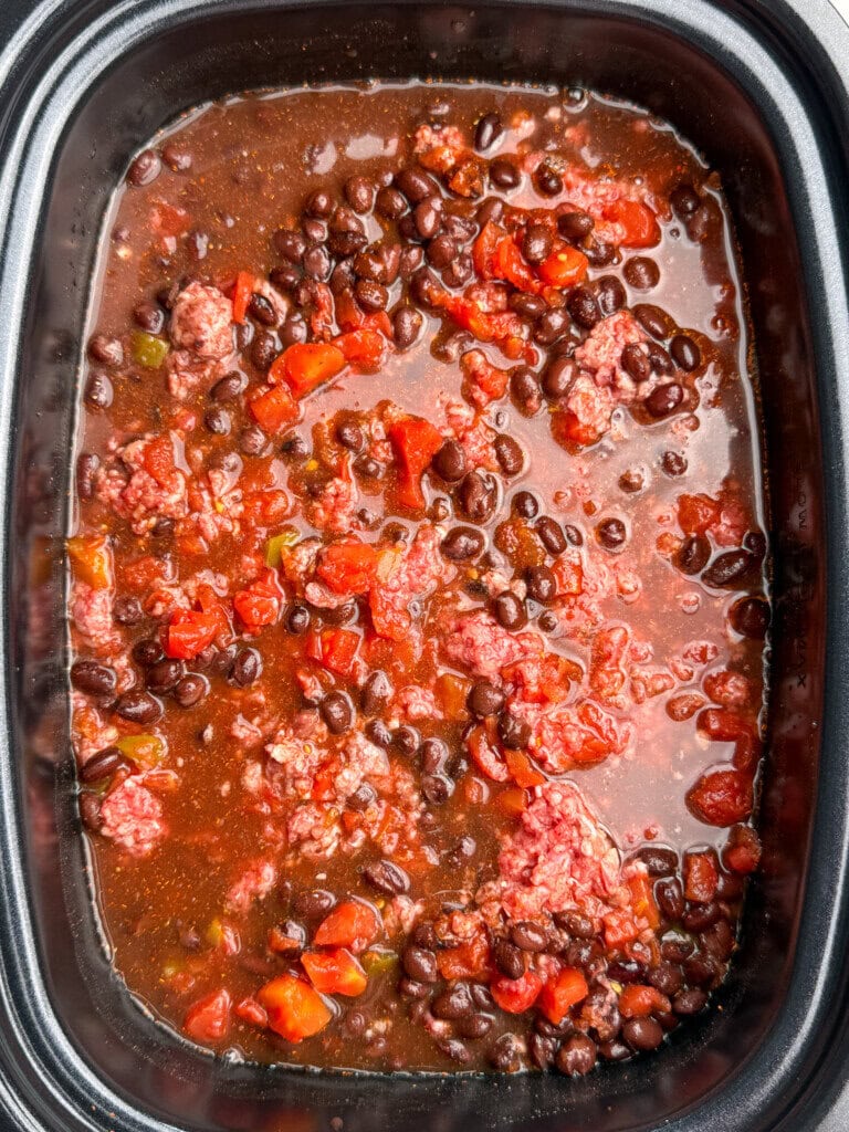A slow cooker filled with a mixture of ground beef, black beans, diced tomatoes, and broth, creating a hearty stew or chili.
