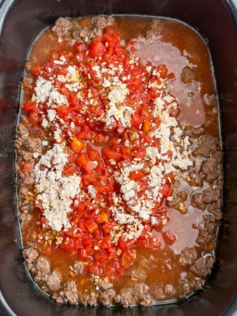Ground beef, diced tomatoes, and seasoning mix in a pot, with visible liquid, ready to be stirred and cooked.
