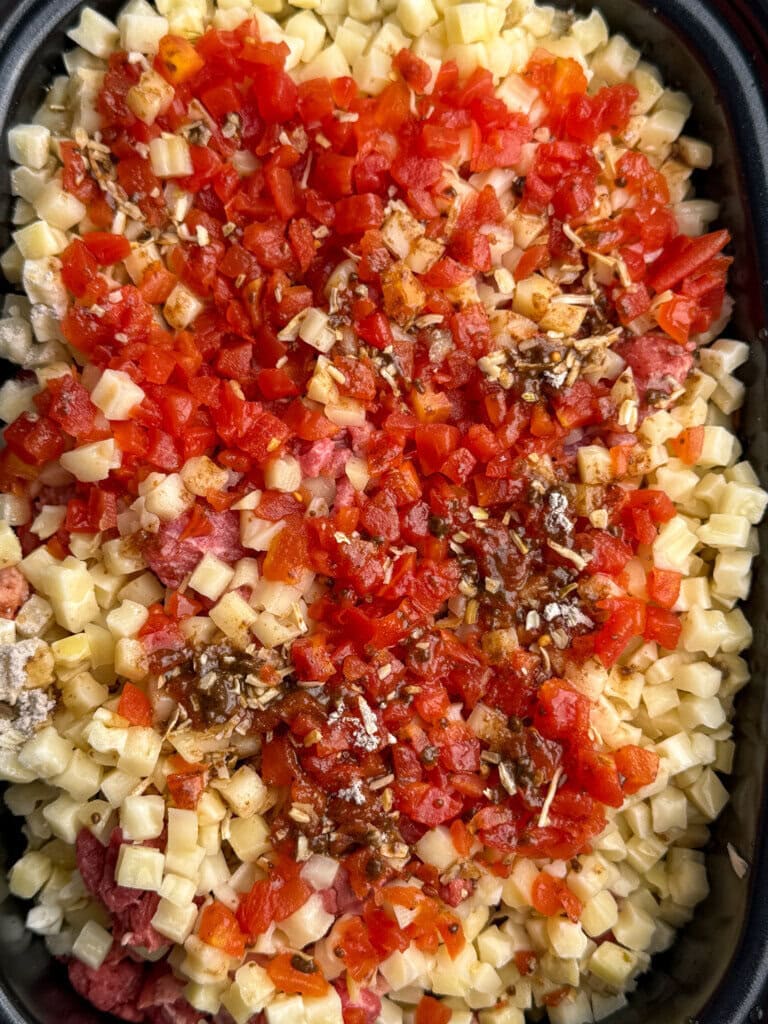 A close-up of a casserole dish filled with diced potatoes, diced
tomatoes, ground meat, and seasonings, ready to be cooked.
