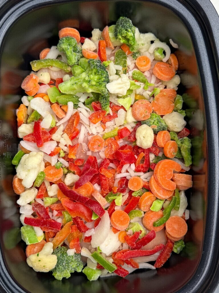 A close-up of a container filled with colorful frozen mixed vegetables, including carrots, broccoli, red peppers, green peppers, and onions.
