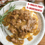 A plate of mashed potatoes topped with Crock Pot Beef Tips With Creamy Onion Gravy sits on a table, garnished with rosemary. Text highlights the recipe as quick to prep and made with just five ingredients.