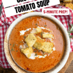 A bowl of Creamy Crock Pot Tomato Soup with Crushed Tomatoes topped with croutons, cheese, and herbs sits next to a spoon on a red checkered cloth. Text reads: Crock Pot Tomato Soup, 5-Minute Prep! Only 7 Ingredients!.